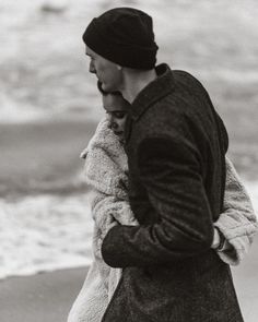 a man and woman walking on the beach with their arms around each other's shoulders