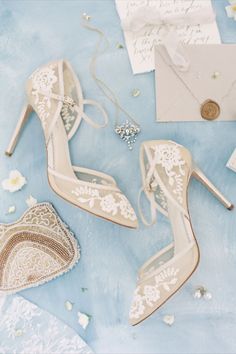 wedding shoes and jewelry laid out on a blue tablecloth with white flowers in the background