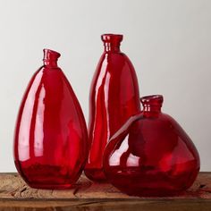 three red glass vases sitting on top of a wooden table next to each other