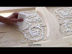 someone is using glue to decorate the wood with white flowers and scrolls on it's surface