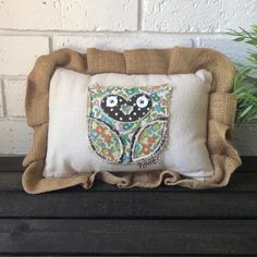 an owl pillow sitting on top of a wooden bench next to a plant and potted plant