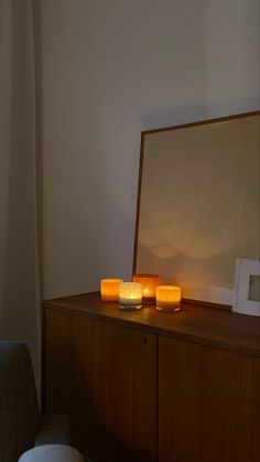 three lit candles sitting on top of a wooden cabinet next to a mirror in a room