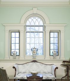 a living room filled with furniture next to two windows and a wooden table in front of it