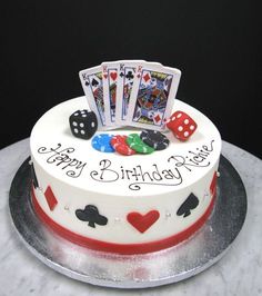 a birthday cake decorated with playing cards, dice and poker chips on a marble table