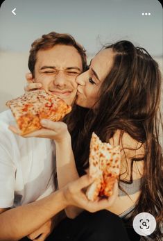 a man and woman sharing a slice of pizza on top of each other in front of the ocean