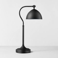 a black lamp on a white table with the light turned on and one arm extended