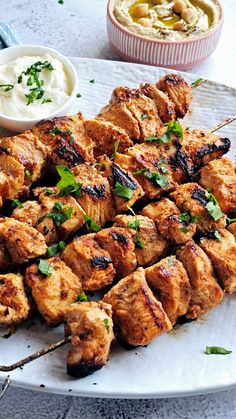 a white plate topped with skewers of meat and vegetables next to a bowl of dip