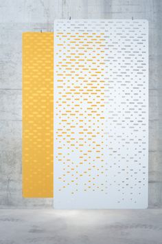 two yellow and white squares are on the wall next to each other in front of a concrete wall