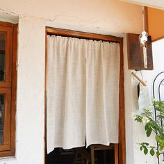 an open window with curtains hanging from the side and a potted plant next to it