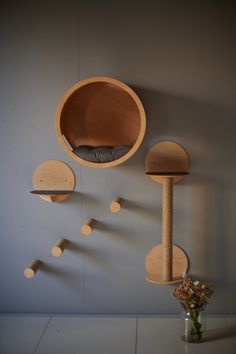 a cat bed and scratching board are hanging on the wall next to a vase with flowers in it