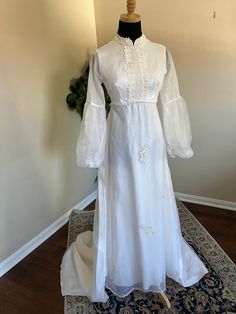 This vintage 1970s wedding dress is a true treasure for a modern-day bride seeking a touch of nostalgia and romance. The dress features a unique and modest design with a detachable train, perfect for adding a touch of drama to your ensemble. In excellent condition, this empire waist dress showcases sheer chiffon bishop sleeves for a delicate and airy feel. Adorned with intricate lace appliques on the bust, neck, waist, and throughout the skirt and train, this dress exudes vintage charm. The full Fitted Vintage Prairie Dress With Bishop Sleeves, Regency Style Empire Waist Prairie Wedding Dress, Gunne Sax Wedding Dress Vintage 70s, 1970’s Wedding Dress, Presley Wedding, Vintage Long Sleeve Cream Prairie Dress, 1970s Wedding Dress, Sleeves Wedding Dress, Wedding Dress Gown