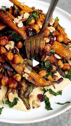 a white plate topped with carrots, nuts and greens next to a fork on top of cheese