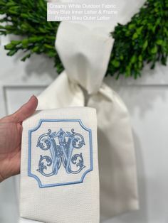 a hand holding up a white cloth with blue trim and a monogrammed initial on it