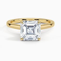 a yellow gold ring with an emerald cut diamond in the center, on a white background