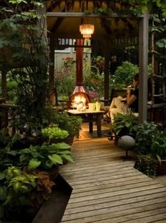 an outdoor patio with a fire pit surrounded by greenery and plants on either side