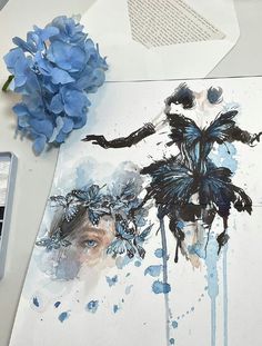 blue flowers are sitting on a table next to an art work with watercolors