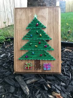 a christmas tree made out of yarn on a wooden plaque in front of a tree