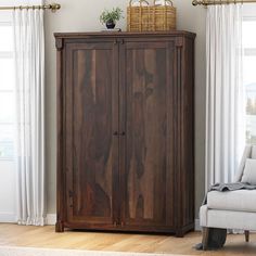 a wooden cabinet sitting in the corner of a living room next to a white chair