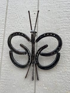 a metal butterfly on the side of a white wooden wall with two black sticks sticking out of it