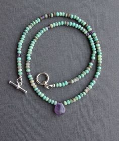 "Chrysoprase and Amethyst Necklace This beaded necklace boasts glorious earthy greens and muted purples, with its combination of chrysoprase and amethyst gemstones. Faceted rondelles of chrysoprase, in all of its natural shades, encircle the neck, sparked with randomly placed amethyst beads. Teardrop amethyst focal pendant. Finished with a sterling silver toggle clasp and findings. Small beads measure about 3.5-4.0mm, and the amethyst drop measures about 11x13mm. Necklace shown measures 18\" in Purple Bohemian Stone Necklaces, Handmade Green Amethyst Gemstones, Bohemian Lavender Hand-strung Jewelry, Green Amethyst Gemstone Beads Jewelry, Green Amethyst Jewelry With Gemstone Beads, Turquoise Amethyst Necklace With Natural Stones, Bohemian Amethyst Necklace With Gemstone Accents, Bohemian Purple Necklace With Gemstone Accents, Green Amethyst Spiritual Necklaces