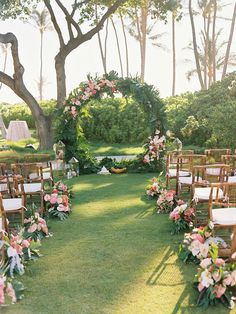 an outdoor ceremony setup with wooden chairs and floral arrangements on the grass, surrounded by trees