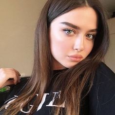 a woman with long brown hair wearing a black t - shirt and looking at the camera