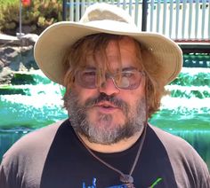 a man wearing a hat and glasses standing in front of a fountain