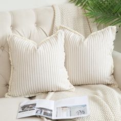 a white couch with two pillows and a book on it next to a palm tree