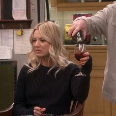 a woman sitting in a chair holding a wine glass with another person standing next to her