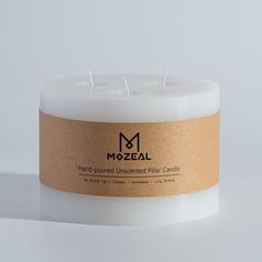 a white candle sitting on top of a table next to a brown paper label that says mozeal