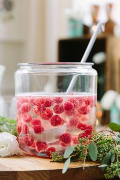 a jar filled with raspberries sitting on top of a wooden table next to flowers