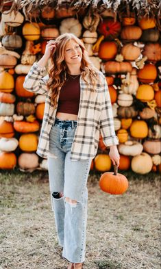 a woman standing in front of a pile of pumpkins