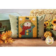 a pillow with a scarecrow on it sitting next to some pumpkins and sunflowers