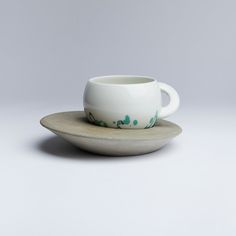 a white cup and saucer sitting on top of a gray plate with green paint splatters