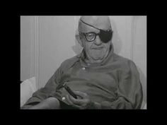 an old man sitting in a chair looking at his cell phone while wearing sunglasses and holding a remote control