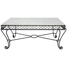 a white marble top coffee table with wrought iron frame and scroll design on the legs