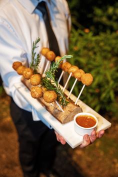 a man is holding a tray with food on it and dipping sauce in the bowl