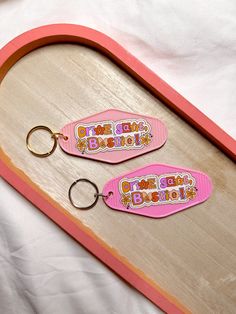 two pink keychains sitting on top of a wooden tray