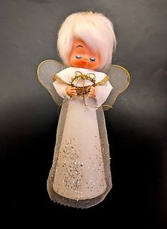 an angel figurine with white hair holding a gold heart and wearing a tiara