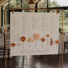 a sign with flowers on it sitting in front of tables and chairs at a wedding