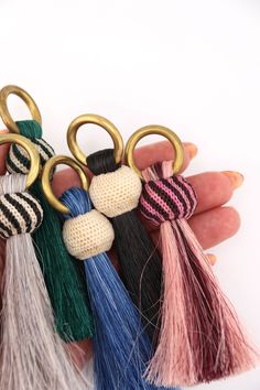 four different colored tasseled keychains in the palm of someone's hand