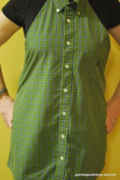 a woman wearing a green and black dress with buttons on the front, standing in front of a yellow wall