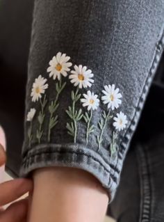 a woman's arm with daisies embroidered on it, while she is holding her hand