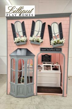 a doll house with windows and flowers in the window boxes on the front, and an ice cream parlor behind it