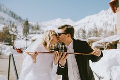 a bride and groom kissing in front of snow covered mountains with skis on them