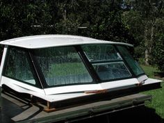 a white boat sitting on top of a grass covered field in front of some trees