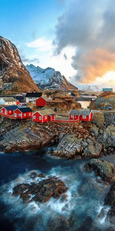 a red house sitting on top of a rocky hill next to the ocean with mountains in the background