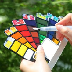 a hand holding a pen and some different colored tiles with one person's finger