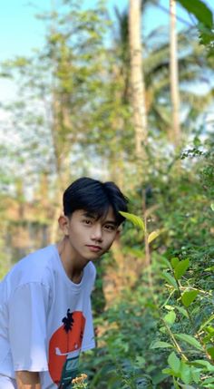 a young man standing in the middle of a forest with lots of trees and plants