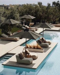 an outdoor swimming pool with lounge chairs and umbrellas on the side, surrounded by olive trees